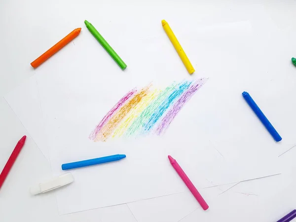 Colored wax crayons on white paper. A rainbow drawn by childrens hands.