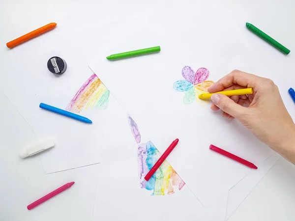 Lápis de cera colorida em papel branco. A mão segura um lápis e desenha uma flor com pétalas coloridas . — Fotografia de Stock