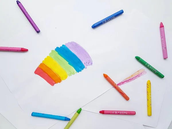 Colored wax crayons on white paper. A rainbow drawn by childrens hands.