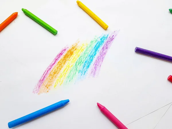 Lápices de cera de colores sobre papel blanco. Un arco iris dibujado por manos de niños . — Foto de Stock
