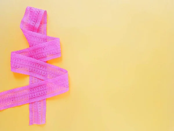 Бавовняна ажурна рожева стрічка складена у вигляді ялинки на жовтому фоні . — стокове фото