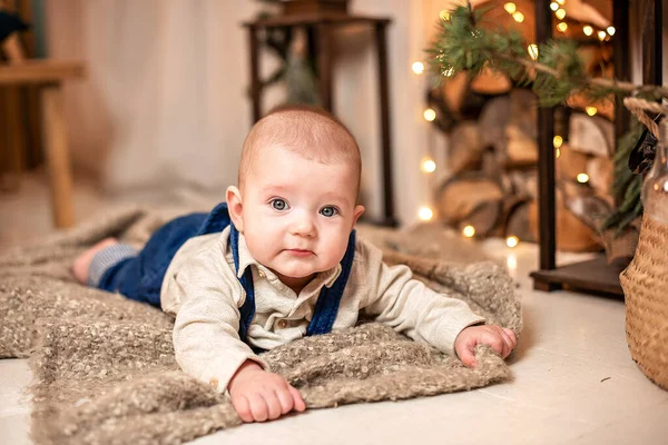 Um pequeno bebê em roupas leves fica no fundo da decoração de Natal . — Fotografia de Stock
