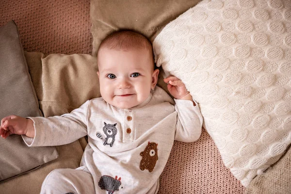 Menino feliz em roupas leves em um sofá com almofadas brancas — Fotografia de Stock