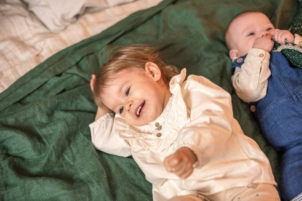 Um irmãozinho e uma irmã felizes em roupas leves estão sorrindo e deitados em um cobertor verde . — Fotografia de Stock