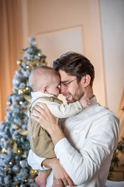 Mutlu bir baba, Noel arkaplanına karşı küçük oğlunu kollarına alır..