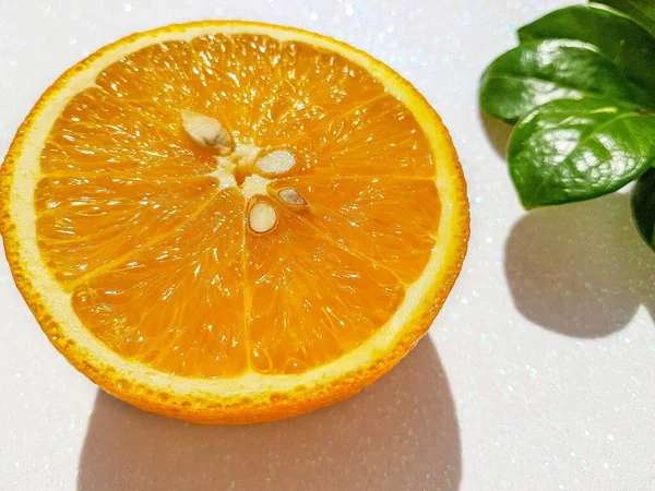 Transverse round cut of a bright juicy orange on a white background with a green zamiokulkas leaf at the back. — Stock Photo, Image