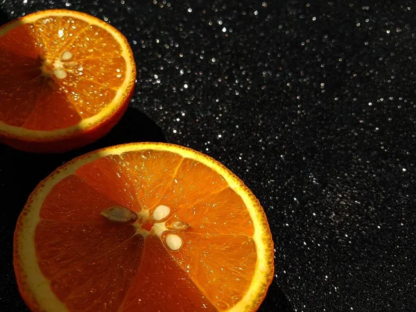 Orange is bright juicy on a black shiny background. Place for the buyers text. A clear shadow passing through the middle of the orange slices. — Stock Photo, Image