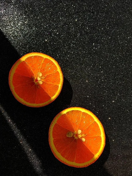 Pomeranč je jasně šťavnatý na černém lesklém pozadí. Místo pro kupující text. Uprostřed oranžových plátků se mihl jasný stín. — Stock fotografie