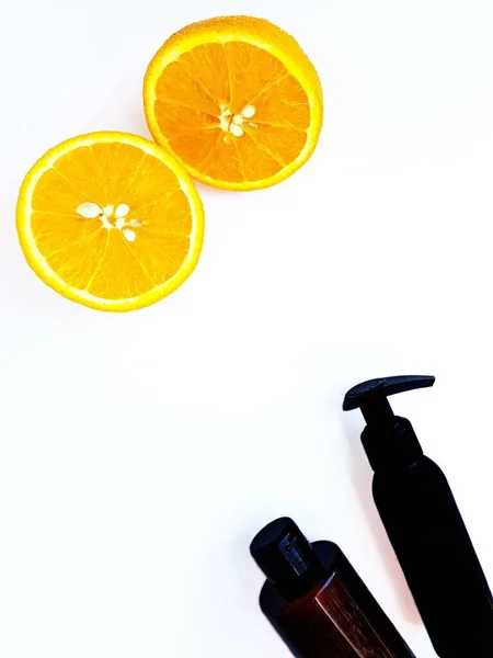 Garrafas cosméticas de plástico preto com uma etiqueta vazia para o layout da marca em um fundo branco com uma laranja suculenta brilhante cortada ao meio. Espaço para texto . — Fotografia de Stock