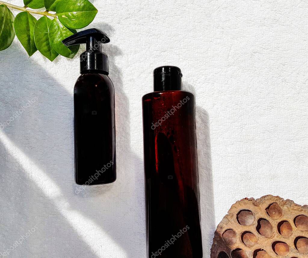 Container cosmetic bottles are white, black, transparent with an empty label for the brand layout on a white background with a green zamiokulkas leaf and a dry Lotus. Space for text.