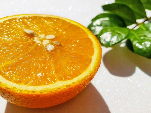 Corte redondo transversal de uma laranja suculenta brilhante em um fundo branco com uma folha zamiokulkas verde na parte de trás . — Fotografia de Stock