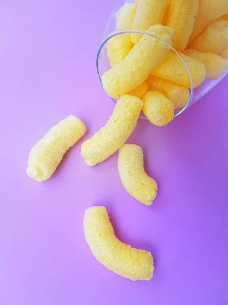 Yellow corn sticks in a high transparent glass on a purple background. — Stock Photo, Image