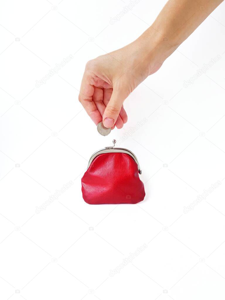 A womans hand puts money in a red purse with a metal lock on a white background. Saving money.