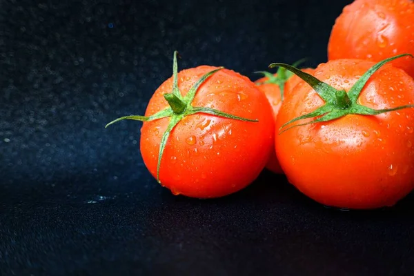 Red ripe juicy tomato with a green stalk with drops of water on a black background close-up. — Stock Photo, Image