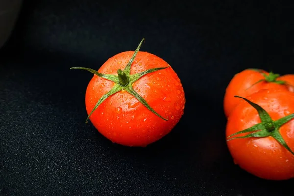 Tomate suculento vermelho maduro com um talo verde com gotas de água em um fundo preto close-up . — Fotografia de Stock