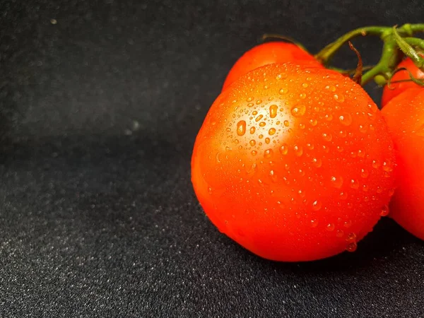 Strahlend saftige rote Tomate auf schwarzem Hintergrund mit Blättern und Stamm. — Stockfoto