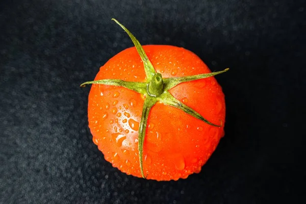 Tomate rojo jugoso brillante sobre un fondo negro con hojas y tronco . — Foto de Stock