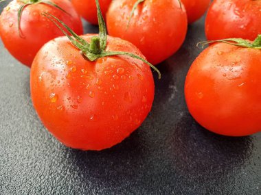 Siyah arka planda yaprakları ve gövdesi olan parlak kırmızı domates..