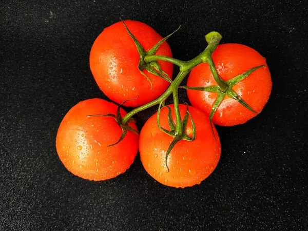 Rote saftige reife Tomate auf grünem Zweig vor schwarzem Hintergrund. — Stockfoto