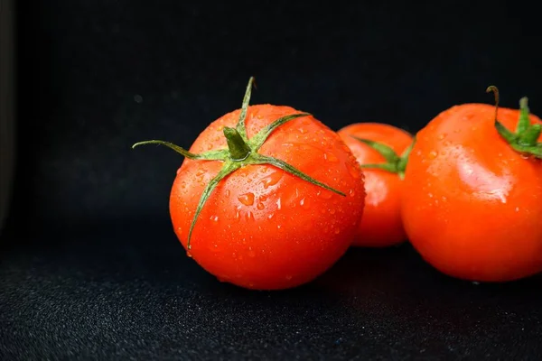 Tomate vermelho suculento brilhante em um fundo preto com folhas e tronco . — Fotografia de Stock