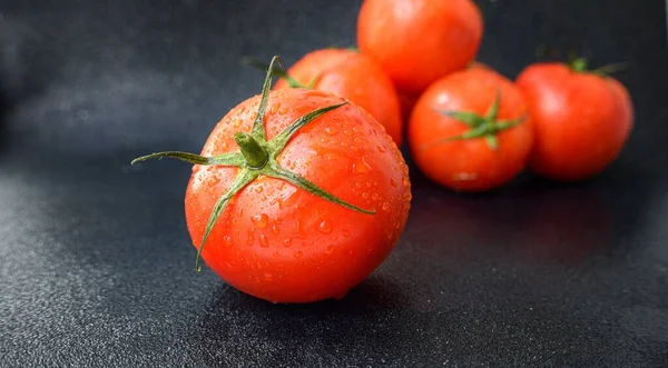 Tomate rouge juteuse mûre avec des feuilles vertes sur un fond sombre. Sur les tomates gouttes d'eau, nettoyer. — Photo