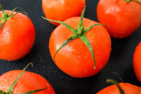 Tomate vermelho suculento maduro com folhas verdes em um fundo escuro. Em gotas de água de tomates, limpas . — Fotografia de Stock