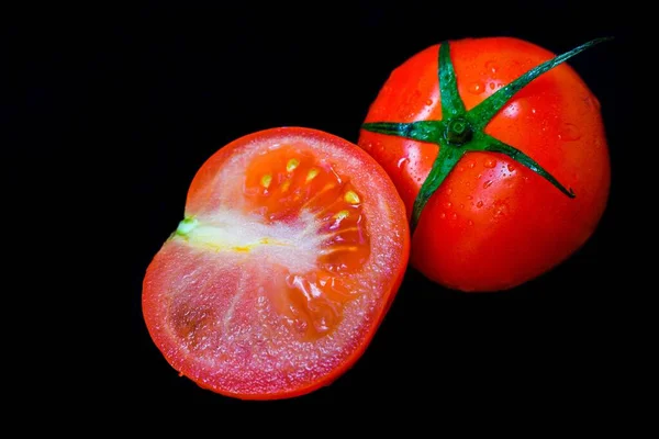 Tomate rojo jugoso maduro con hojas verdes sobre un fondo oscuro. Sobre los tomates gotas de agua, limpiar . — Foto de Stock