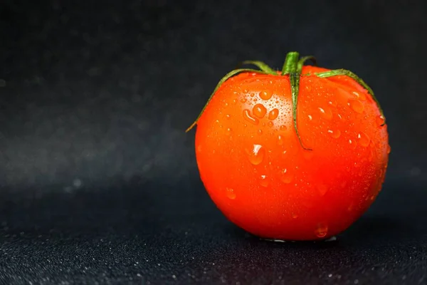 Tomate rojo maduro sobre fondo negro con gotas de agua después del lavado . — Foto de Stock