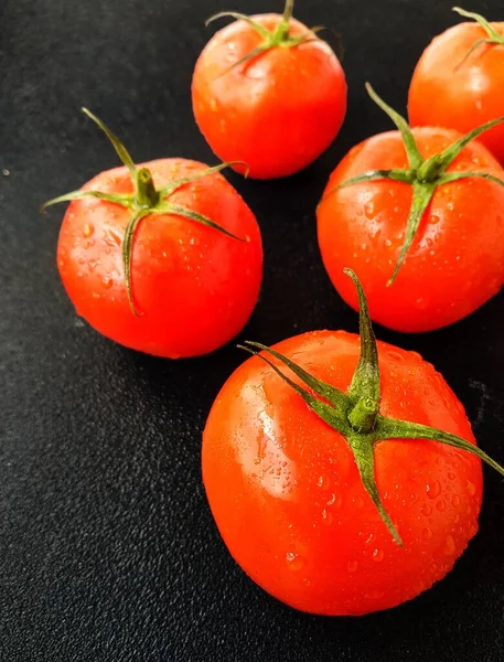 Tomate vermelho suculento maduro com folhas verdes em um fundo escuro. Em gotas de água de tomates, limpas . — Fotografia de Stock