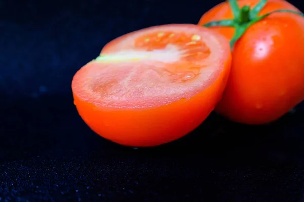 Tomate rojo jugoso maduro con hojas verdes sobre un fondo oscuro. Sobre los tomates gotas de agua, limpiar . —  Fotos de Stock