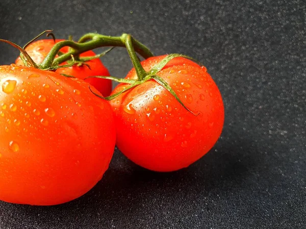 Tomate rojo jugoso maduro con hojas verdes sobre un fondo oscuro. Sobre los tomates gotas de agua, limpiar . — Foto de Stock