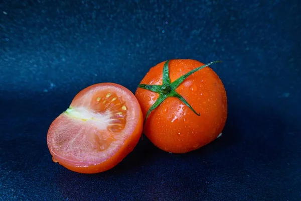 Tomate vermelho suculento maduro com folhas verdes em um fundo escuro. Em gotas de água de tomates, limpas . — Fotografia de Stock