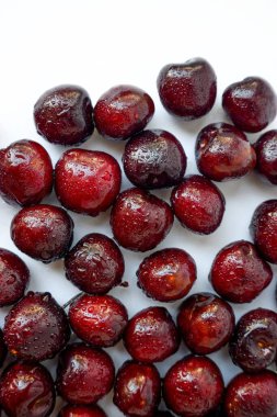 Beyaz bir zemine serpiştirilmiş kırmızı kiraz ve bir damla su..