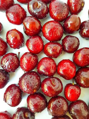 Beyaz bir zemine serpiştirilmiş kırmızı kiraz ve bir damla su..