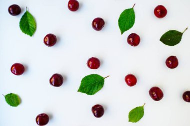 Beyaz arka plana serpilmiş yeşil yapraklı parlak kırmızı sulu olgun kiraz..
