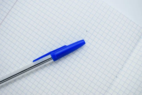Bolígrafo con una gorra azul en el cuaderno de la escuela en una jaula sobre un fondo blanco . — Foto de Stock