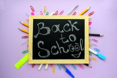 Siyah bir okul yönetim kurulunda, mor bir arkaplan ve kırtasiyede ahşap çerçeve ile okula dönüş metni..