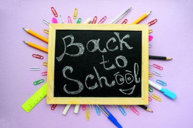 Siyah bir okul yönetim kurulunda, mor bir arkaplan ve kırtasiyede ahşap çerçeve ile okula dönüş metni..