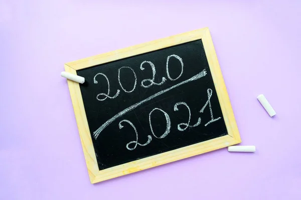 Inskription 2020 2021 krita på en svart tavla med en träram på en lila bakgrund och brevpapper. — Stockfoto