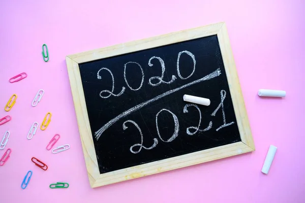 Inskription 2020 2021 krita på en svart tavla med en träram på en lila bakgrund och brevpapper. — Stockfoto