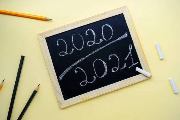 Inscrição 2020 2021 giz em uma placa preta com uma moldura de madeira em um fundo amarelo e artigos de papelaria . — Fotografia de Stock