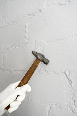 Beyaz eldivenli bir kadın bir çekiç tutuyor ve beyaz bir tuğla duvara vuruyor. Dairenin tadilatı