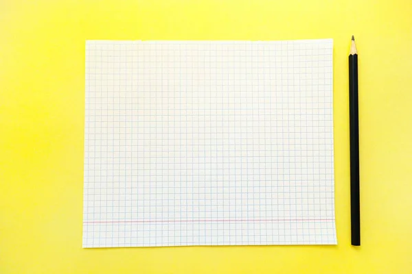 A white sheet of notebook paper in a cage on a bright yellow background with a black slate pencil. — Stock Photo, Image