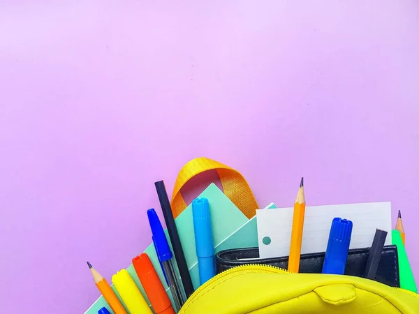 Szkolny żółty plecak z notatnikami i materiałami szkolnymi na fioletowym tle. Wracamy do szkoły.. — Zdjęcie stockowe