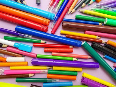 Mor arka planda dağılmış kalemler ve işaretler. Okul malzemeleri. Okula geri dön..