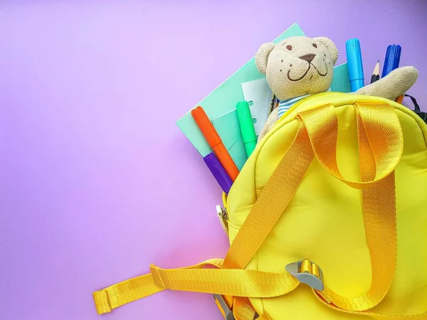 Mochila amarela escolar com cadernos e material escolar em fundo roxo. De volta à escola . — Fotografia de Stock