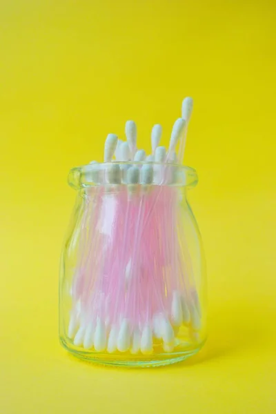 Telinga tongkat plastik kapas merah muda pada latar belakang kuning dalam stoples kaca. kebersihan pribadi dan kepedulian. Kosmetologi dan obat. — Stok Foto