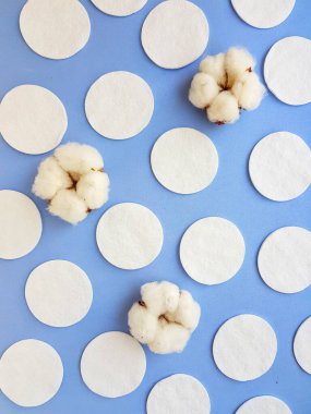 Yuvarlak pamuk diskler ve pamuk çiçekleri parlak mavi arkaplanda.