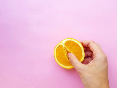 A vagina symbol. The concept of sex. Finger on an orange on a pink background.
