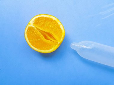 The concept of safe sex and protection. A vagina symbol. A juicy orange and a condom on a bright blue background.